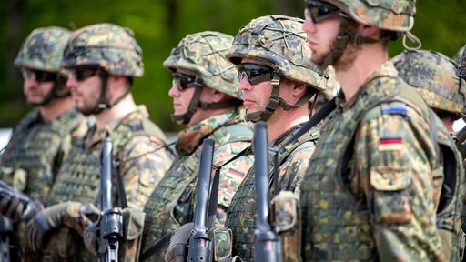 Mehrere Soldaten stehen mit Waffen in Uniform nebeneinander.