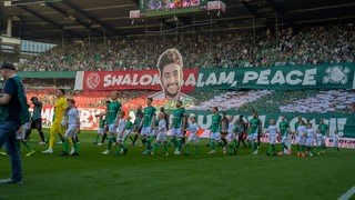 Die Spieler von Werder Bremen laufen mit Einlaufkindern an der Hand vor der Fan-Choreografie in Gedenken an Hersh Goldberg-Polin ins Weser-Stadion.