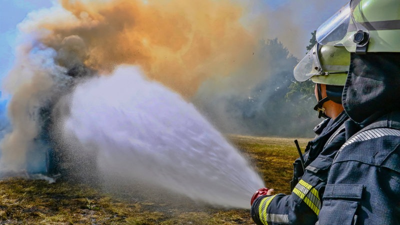 Zwei Feuerwehrleute löschen brennende Heuballen.