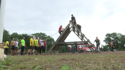 Teilnehmer eines Hindernislaufes beim klettern über ein Holzgerüst