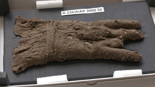 Ein antiker Handschuh aus Stoff liegt in der Landesarchäologie Bremen aus