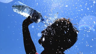 Bei strahlend blauem Himmel und tropischen Temperaturen schüttet sich ein Junge Wasser aus einer Flasche über seinen Kopf.