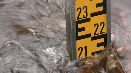 Ein Pegelstab wird während einer Überschwemmung von Wasser umspüllt