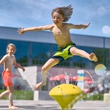 Kinder springen im Horner Freibad über Wasserspiele.