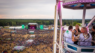 Blick aus der Gondel eines Riesenrads auf Besucher des Hurricane Festivals und das Festivalgelände.
