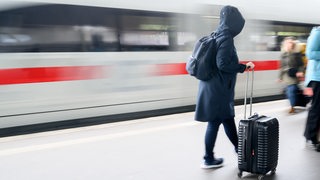 Eine Frau steht mit einem Koffer auf dem Bahnsteig im Hauptbahnhof Hannover, während ein ICE einfährt