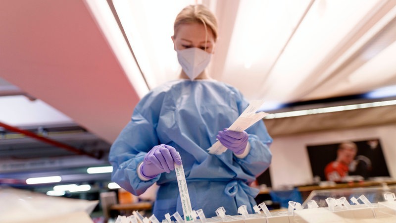 A woman in protective clothing takes corona tests from packs.