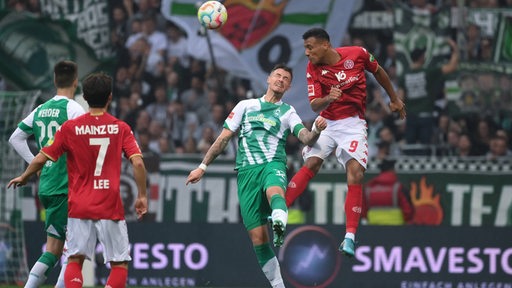 Mainz-Stürmer Karim Onisiwo und Werder-Verteidiger Marco Friedl kämpfen in der Luft um den Ball.