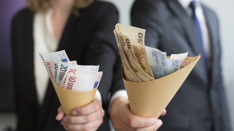Gender Pay Gap: Eine Frau und ein Mann halten unterschiedlich gefüllte Lohntüten mit Euros in die Kamera