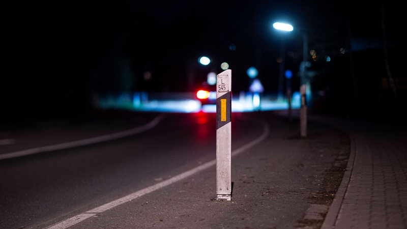 Eine leere dunkle Straße mit einem Leitpfosten im Vordergrund.