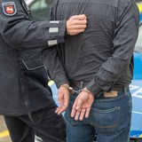 Ein Polizist führt einen Mann ab. Die beiden sind von hinten zu sehen.