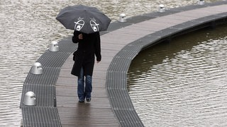 Eine Person mit Regenschirm läuft auf einem Steg an den Bremer Wallanlagen.