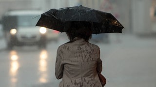 Eine Person steht durchnässt auf einer Straße und hält einen Regenschirm.