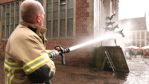 Ein Feuerwehrmann spritzt die Stadtmusikanten sauber.