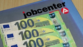 Vier 100-Euro-Scheine liegen auf einer Mappe mit der Aufschrift "Jobcenter"