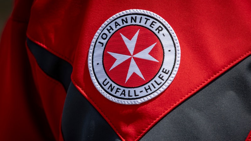 Das Logo der Johanniter-Unfall-Hilfe ist auf einer roten Jacke zu sehen.