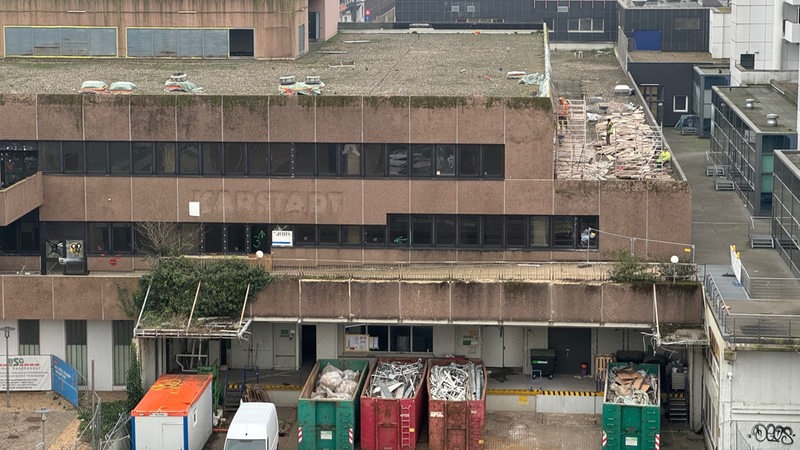 Bauarbeiter arbeiten an einer Betonfassade eines Gebäudes, das den verblassten Schriftzug "Karstadt" trägt.