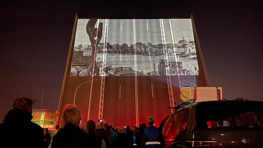 Eine hochgeklappte Straßenbrücke, auf ihr sind Fotos projiziert.