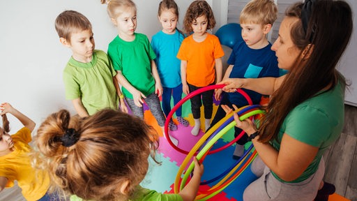 Eine Kindergruppe mit Erzieherin, die Spielreifen verteilt.