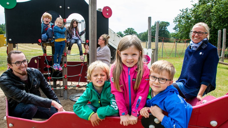 Drei Erzieherinnen und Erzieher betreuen Kinder auf einem Spielplatz.