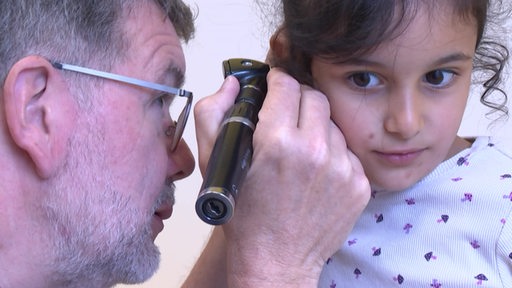 Ein Arzt misst bei einem Mädchen im Ohr Fieber.