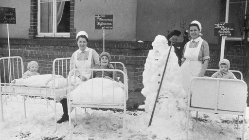 Kranke Kinder liegen auf ihren Betten vor dem Krankenhaus. Es hat geschneit.