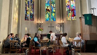 Besucher sitzen mit Tisch und Stühlen im Altarraum einer Kirche.