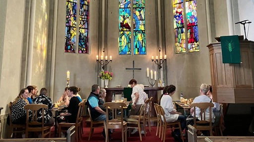 Besucher sitzen mit Tisch und Stühlen im Altarraum einer Kirche.