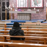 Eine Person in Winterkleidung sitzt in einer Kirchenbank und blickt zum Altar.