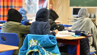 Schülerinnen und Schüler arbeiten im Klassenzimmer in warmer Kleidung.