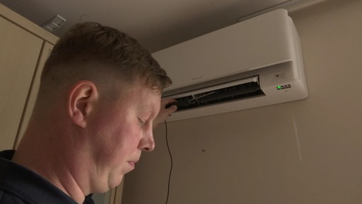 Ein Klimatechniker checkt die Klimaanlage an der Zimmer-Wand.