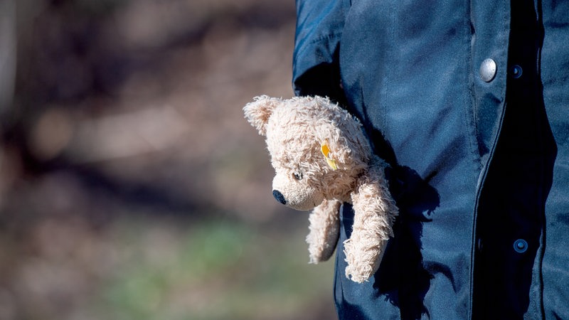 Ein Teddybaer ragt aus der Manteltasche einer Frau