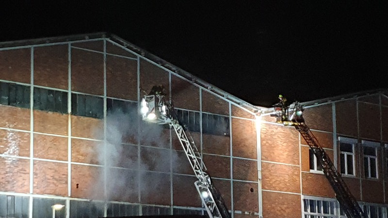 Feuerwehrleute stehen auf einer Drehleiter und löschen eine Lagerhalle. 