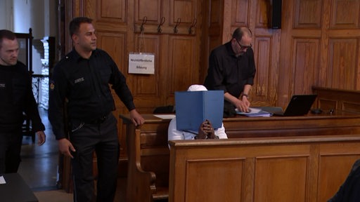 Der Angeklagte mit einer blauen Mappe vor dem Gesicht im Bremer Landgericht.