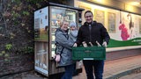 Eine Frau und ein Mann stehen mit einem Kleinkind und einer Kiste vor einem Automaten.