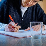 Ein Mann sitzt an einem Tisch und streicht mit einem roten Stift etwas an.