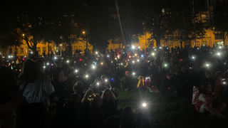 Eine Gruppe von Menschen sitzt im Dunkeln auf einer Wiese und erleuchten diese mit Taschenlampen und Lichterketten.