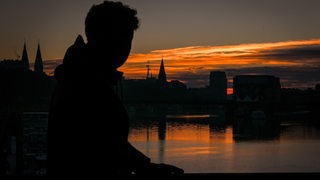 Ein Mann beobachtet den Sonnenaufgang an der Weser in Bremen, die Stadt liegt (noch) im Dunklen.