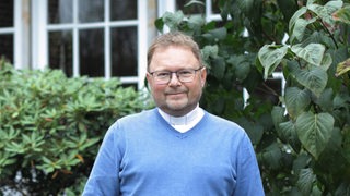 Pastor Andreas Hamburg steht vor Büschen bei der Markusgemeinde in Bremen Arsten