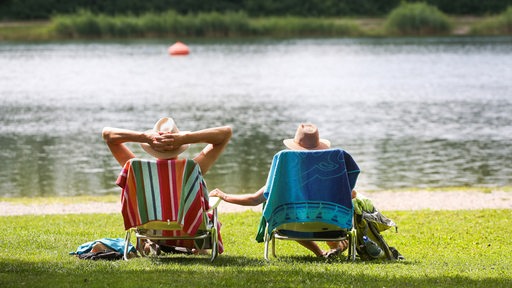 Menschen sitzen in einem Liegestuhl und schauen auf einen See