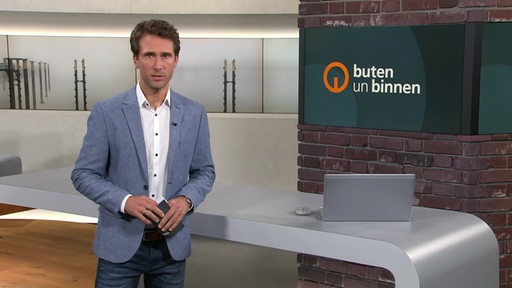 Moderator János Kereszti steht im Studio von buten un binnen vor einem Pult.