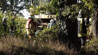 Feuerwehrleute stehen auf einem Feld vor einem Maishäcksler.