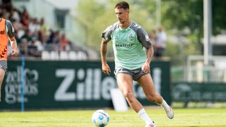 Werder-Kapitän Marco Friedl trägt ein Trainingsshirt und hat den Ball auf dem Platz am Fuß