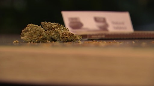 Auf einem Tisch liegen Cannabisknollen und Blättchen zum Joint drehen.