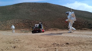 Zwei Astronauten mit Fahrzeug in Wüstenlandschaft