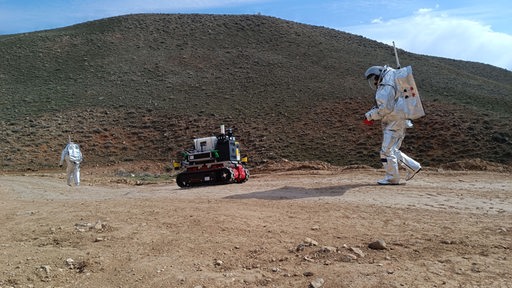 Zwei Astronauten mit Fahrzeug in Wüstenlandschaft