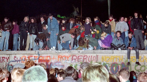 Einen Tag nach der Grenzöffnung in Berlin feiern tausende Menschen auf, vor und hinter der Berliner Mauer am Brandenburger Tor, aufgenommen am 10. November 1989 auf West-Berliner Seite.