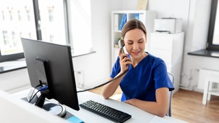 Eine medizinische Fachkraft sitzt an einem Schreibtisch und telefoniert