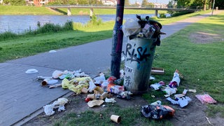 Ein Mülleimer am Werdersee ist überfüllt. Um den Mülleimer liegen mehre Plastiktüten, Pappbecher udn weiterer Müll. 