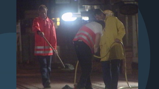 Drei Bauarbeiter arbeiten nachts auf einer Baustelle.